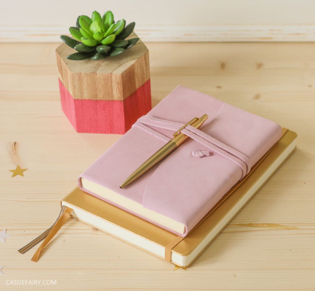 office desk with pink notebook, gold notebook and gold pen 