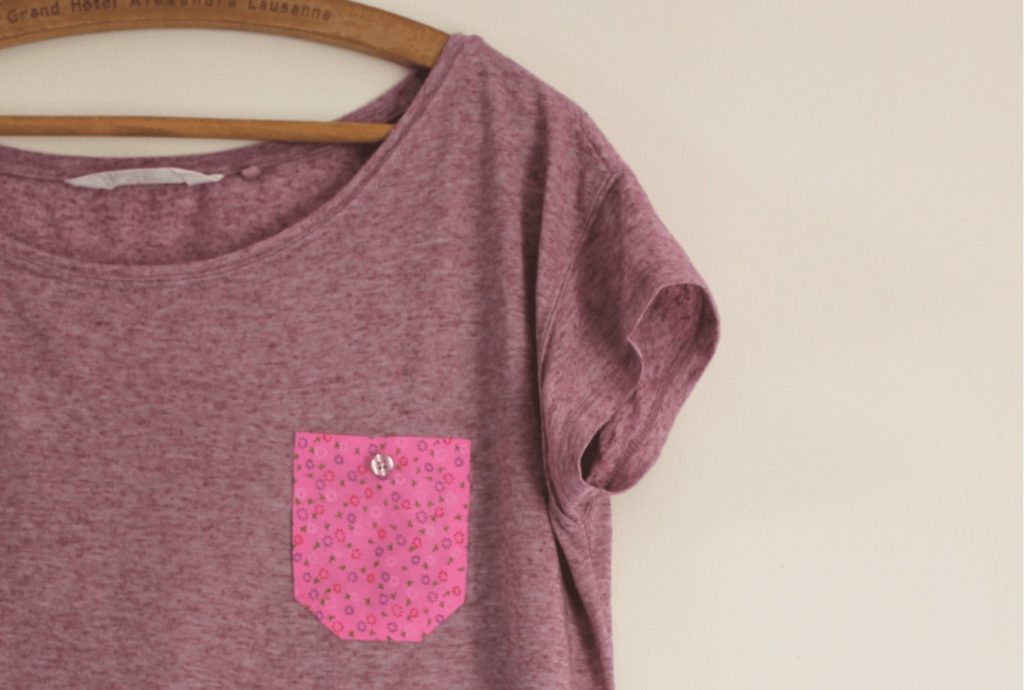 Photo of a purple t-shirt with contrasting applique pocket hanging on a coat hanger