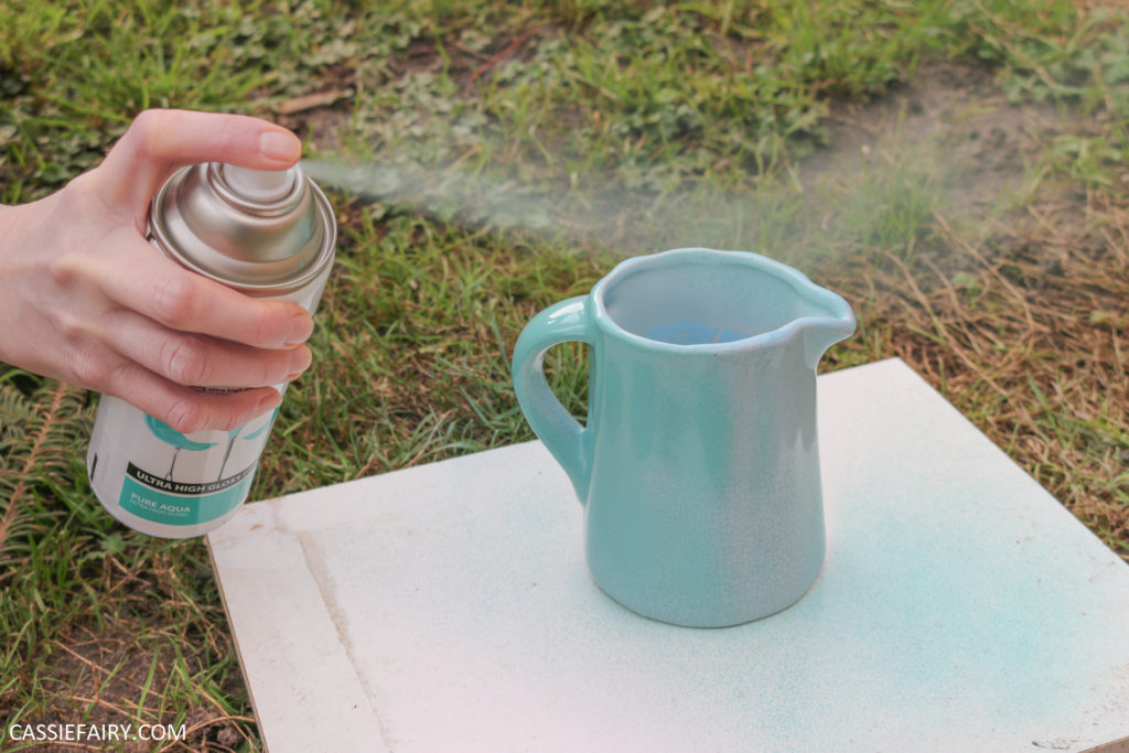 spray painting a small jug with turquoise paint