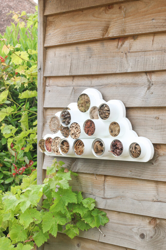 Image shows a cloud-shaped bug hotel made from tin cans attached to the side of a shed