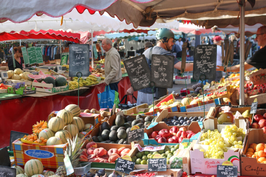 Image of a fruit stall at a French open-air market showing melons, peaches, grapes, oranges and plums.