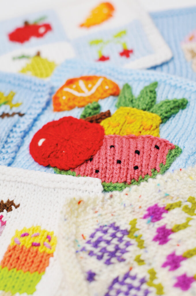 Knitted intarsia and crochet motifs of fruit including an apple, watermelon slice, pineapple and orange slice