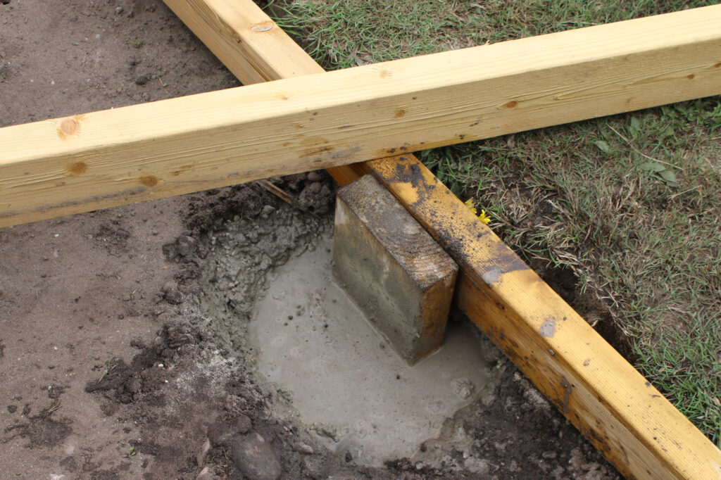 A hole filled with concrete, setting a support post into the ground.