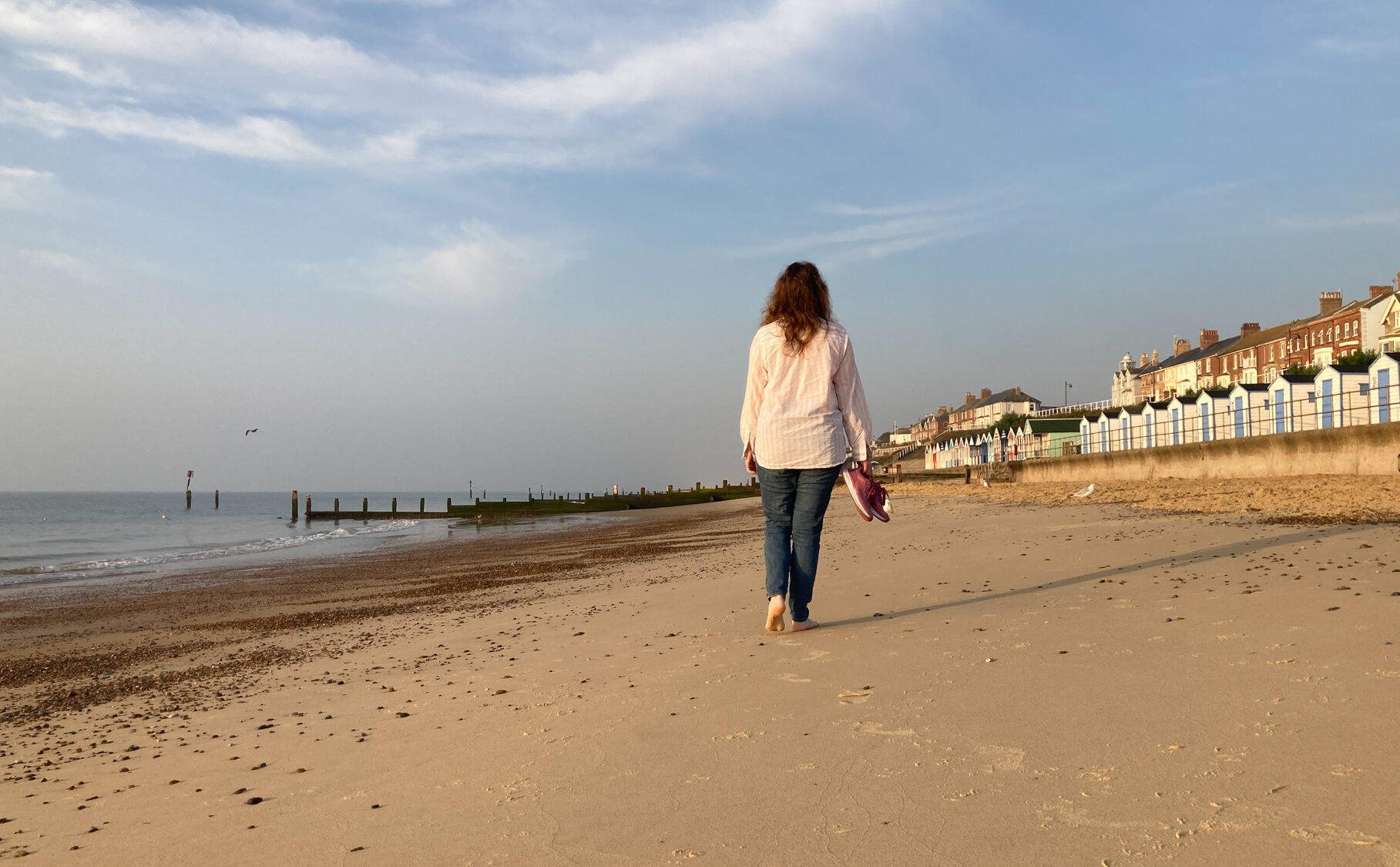 A female figure walking along a sandy beach with gentle waves lapping the shore.