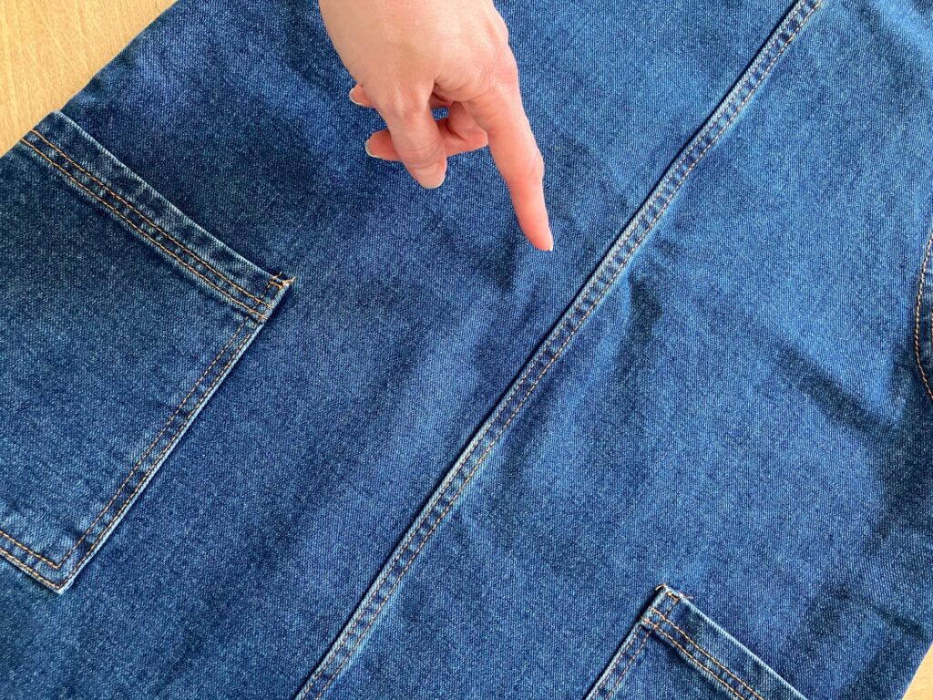 A hand pointing out a stain on a denim dress.