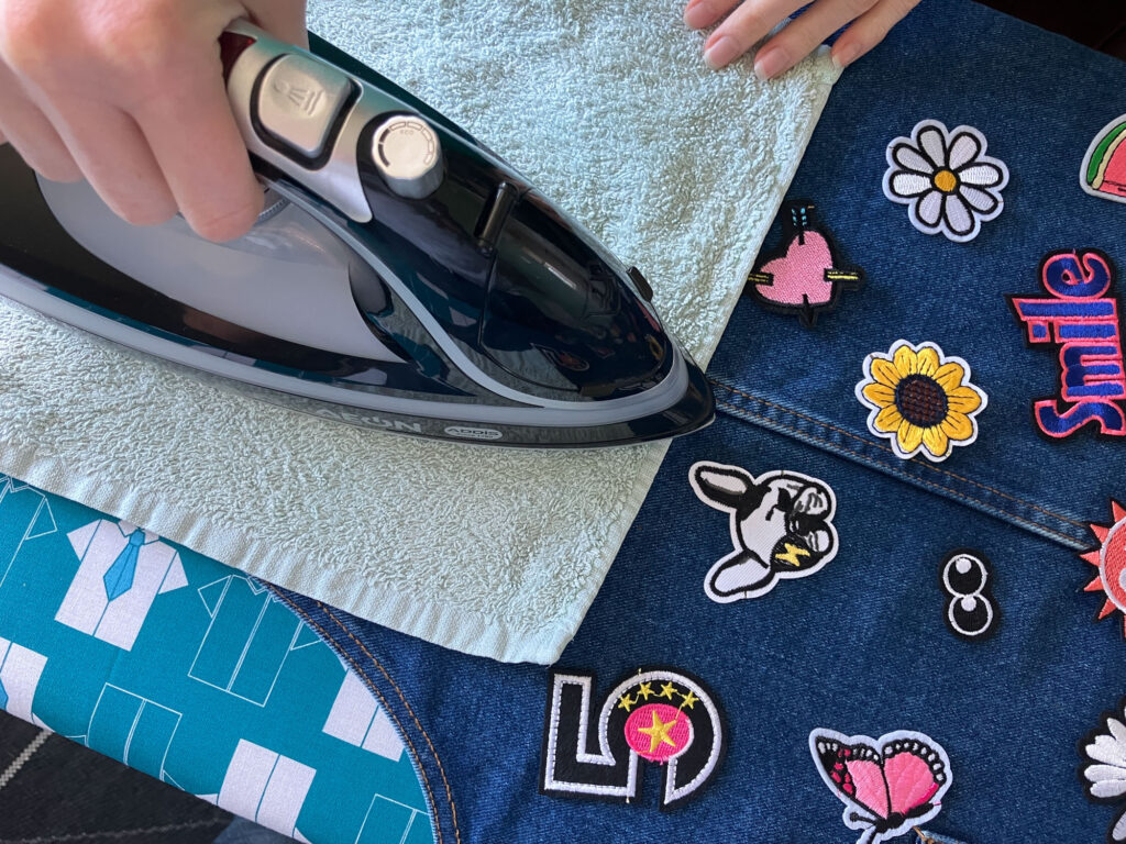 Hands ironing colourful embroidered patches onto a denim dress.