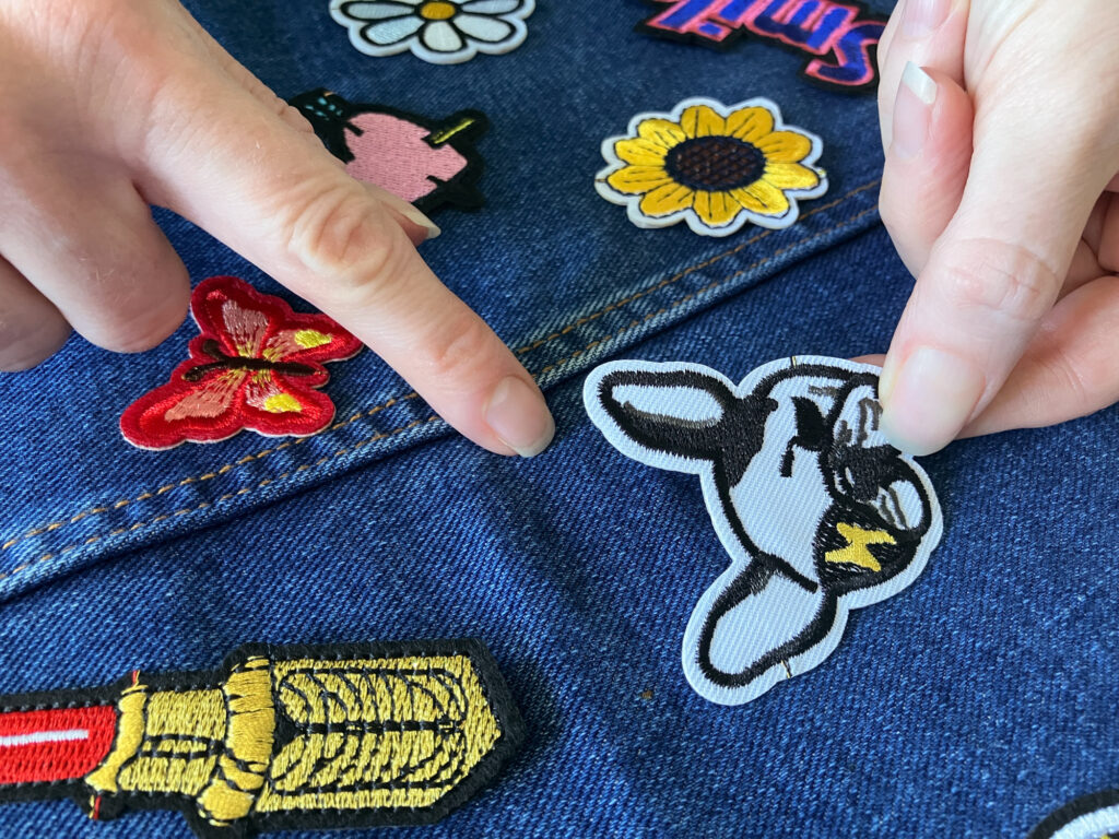 Hands positioning colourful embroidered patches onto a denim dress to cover stains.