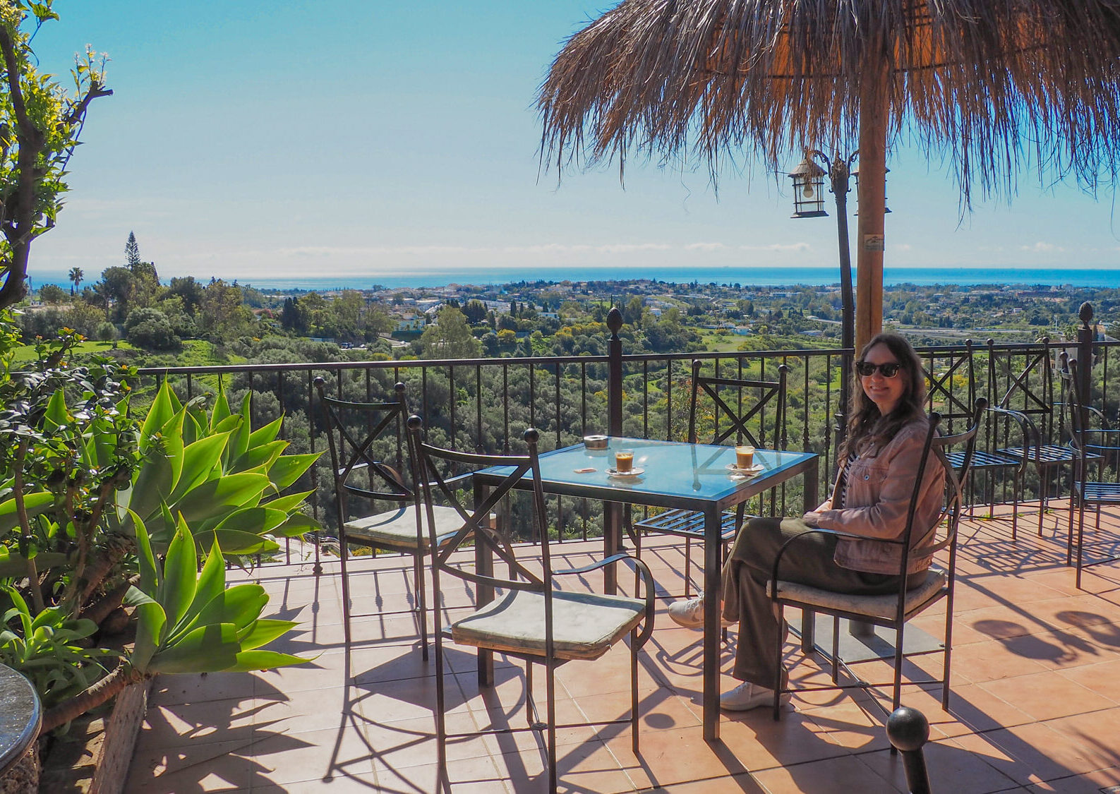 A digital nomad enjoying a coffee at an outdoor table overlooking a view of the Malaga coastline in Spain.