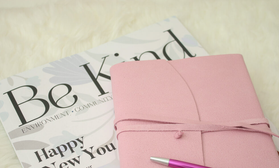 A pink journal and pen on top of a wellbeing magazine titled "Be Kind". 