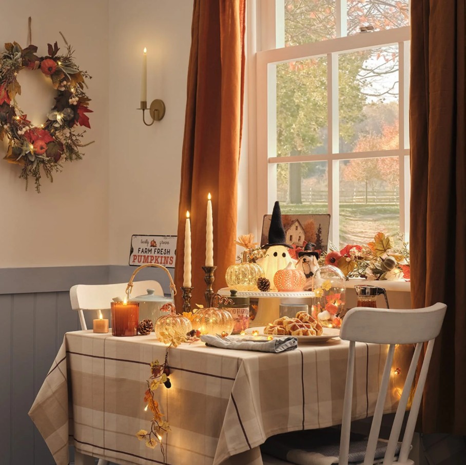 A table for two covered in a checked tablecloth, decorated with light-up pumpkins and ghosts and all candlesticks, with a plate of waffles.