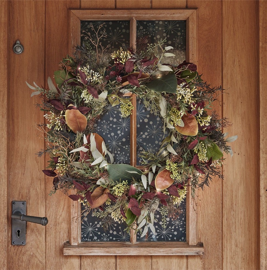 A pre-lit exterior wreath with faux autumn foliage on a wooden door.