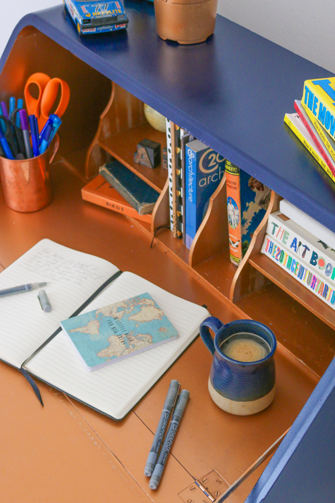 Inside the finished desk with a copper interior, styled with a notebook and blue cup of coffee.
