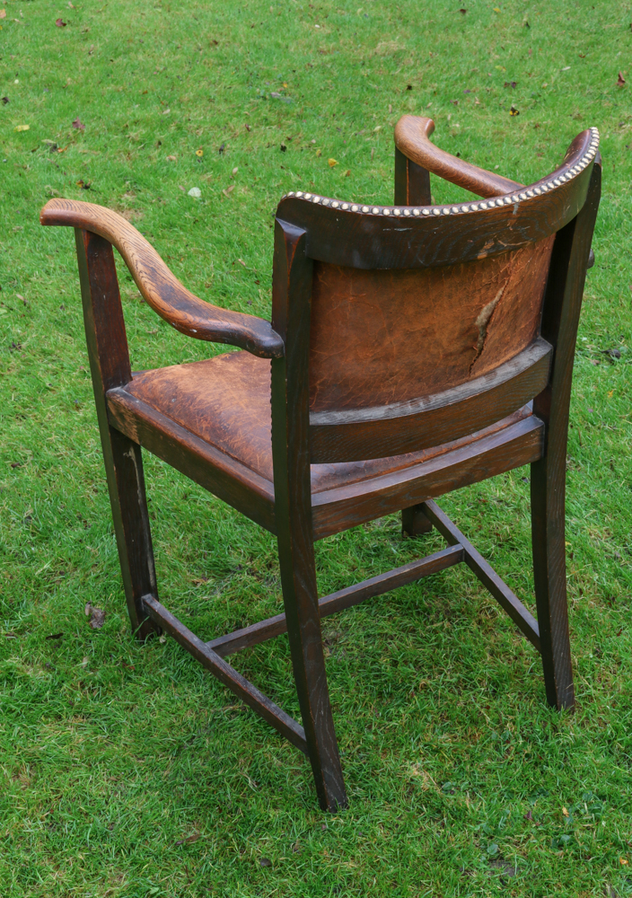 The back of a leather chair with a wooden frame, with a large tear on the back of the leather panel.