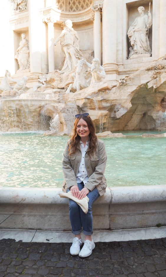 A woman sitting on the edge of the Trevi Fountain.